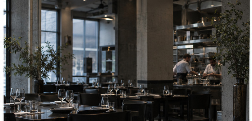 La salle, ses tables dressées et la cuisine ouverte au fond